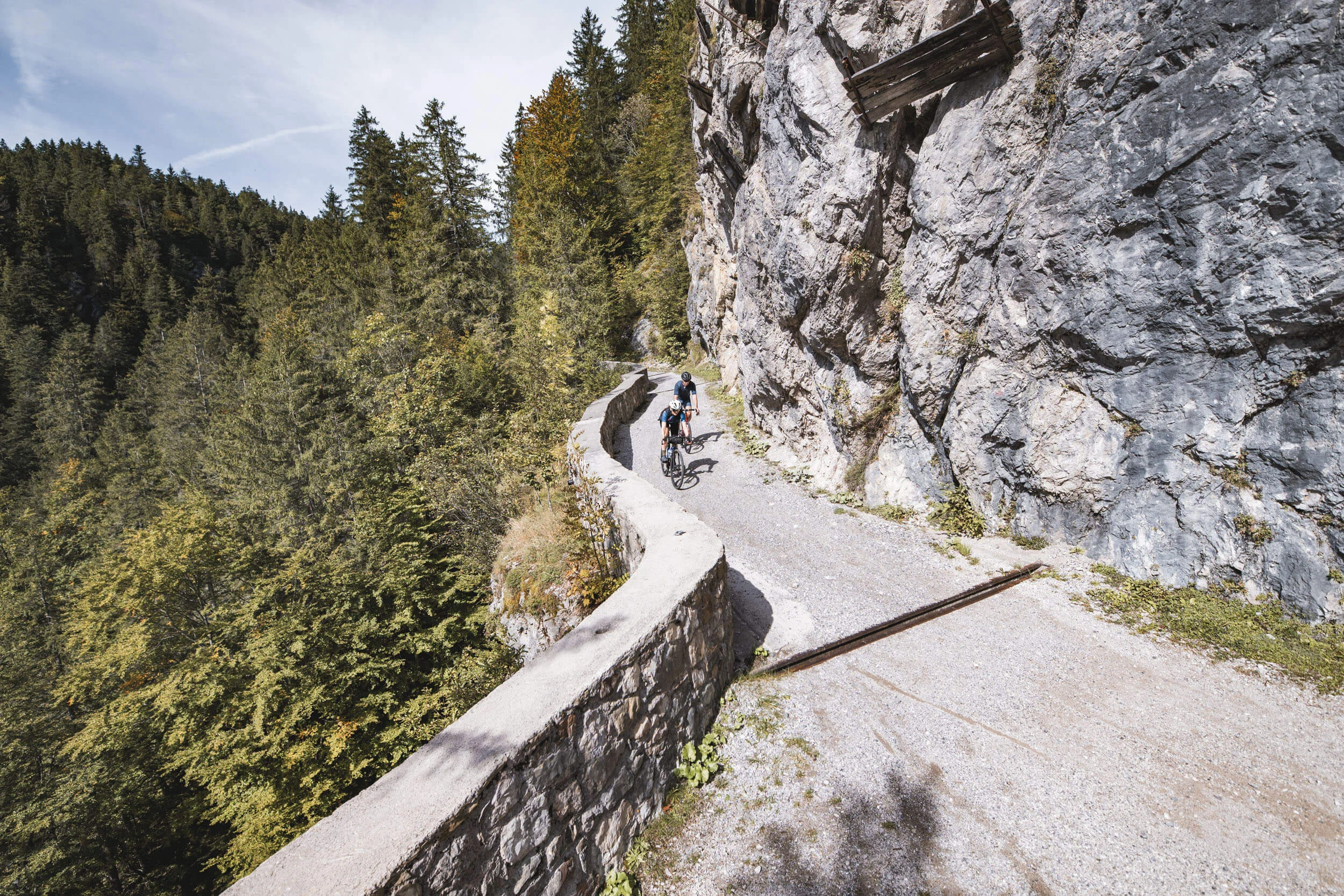 Alpine Graveln © Andreas Vigl Zwei Radfahrer auf schmalem Bergweg neben Felswand und Wald