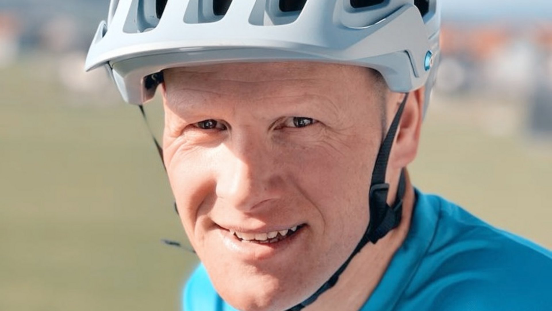 Nahaufnahme eines lächelnden Mannes mit weißem Fahrradhelm und blauem Shirt