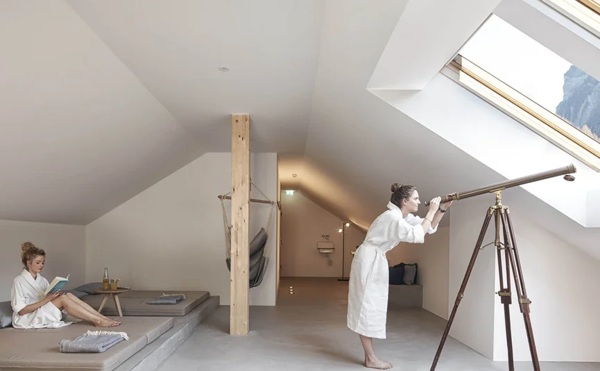 Frau im Bademantel beobachtet mit Teleskop durch Dachfenster in modernem Raum