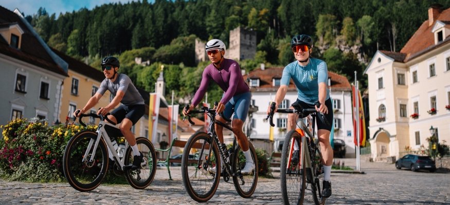 Stift St. Georgen **** © Martin Hoffmann Drei Radfahrer auf Kopfsteinpflaster in einer Stadt mit Bergen im Hintergrund