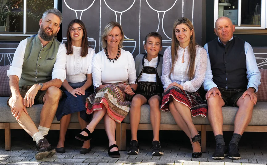 Familie in traditioneller Tracht sitzt auf einer Bank vor einer bemalten Wand