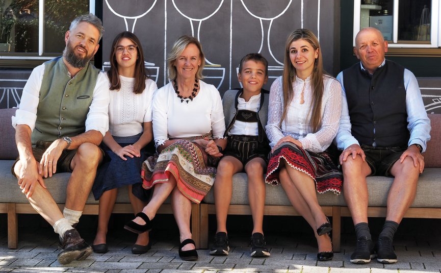 Hotel Ostaria Posta *** © Ueberall GmbH Familie in traditioneller Tracht sitzt auf einer Bank vor einer bemalten Wand