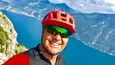 Mann mit rotem Fahrradhelm macht Selfie vor Berg und See