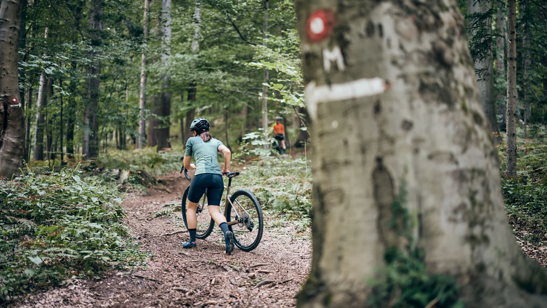 Radfahrer schiebt Mountainbike auf Waldweg den Hügel hinauf