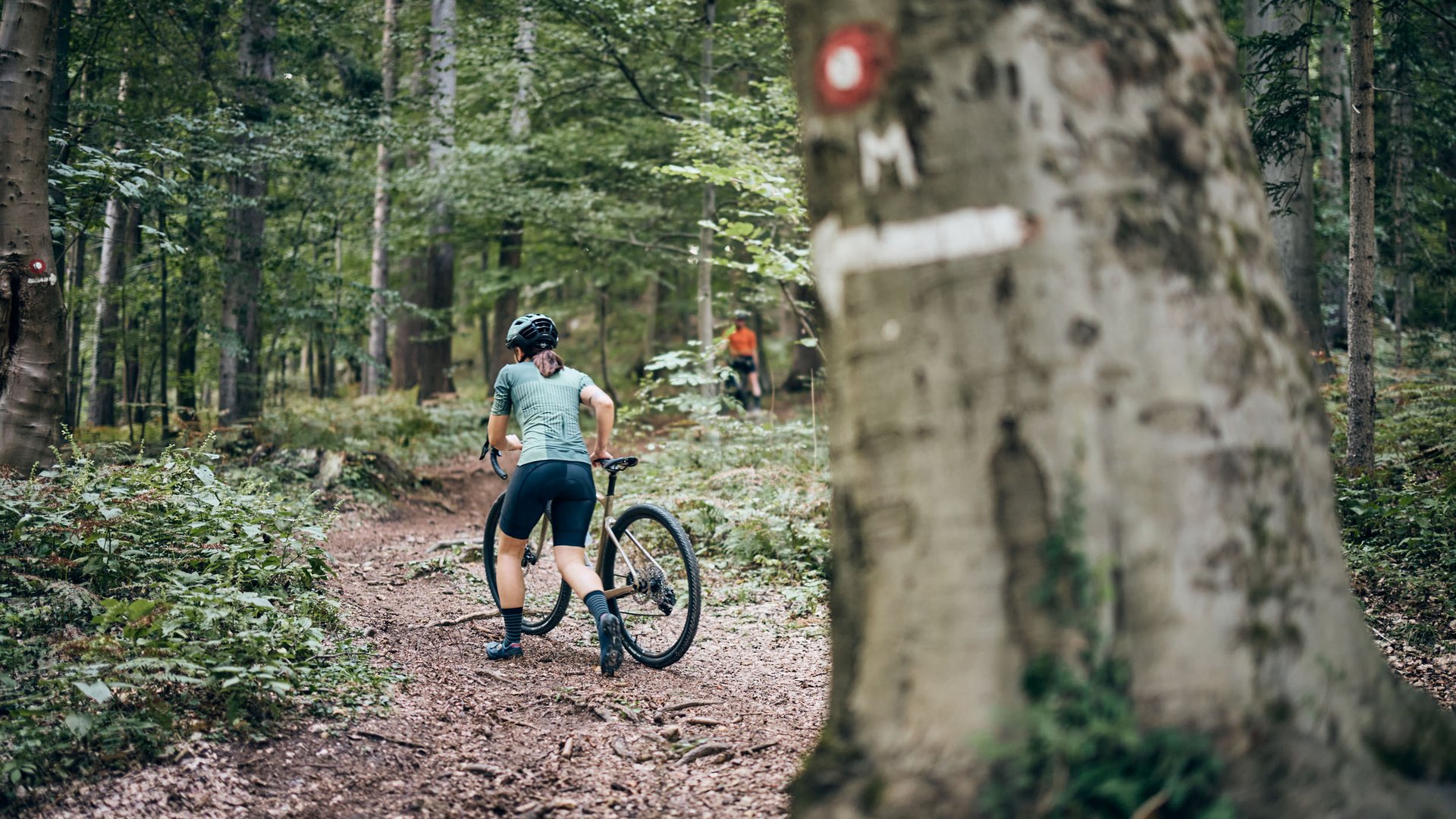 Radfahrer schiebt Mountainbike auf Waldweg den Hügel hinauf