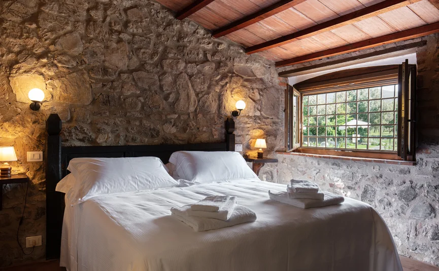 Tenuta Il Cicalino © Tenuta il Cicalino Gemütliches Schlafzimmer mit Steinwand und offenem Fenster zur grünen Landschaft