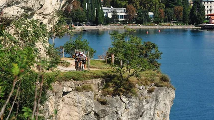 Two cyclists on cliff-edge trail overlooking lake and town in background