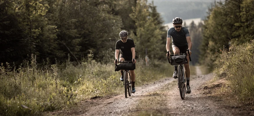 Zwei Radfahrer fahren auf einem Waldweg bei bewölktem Himmel