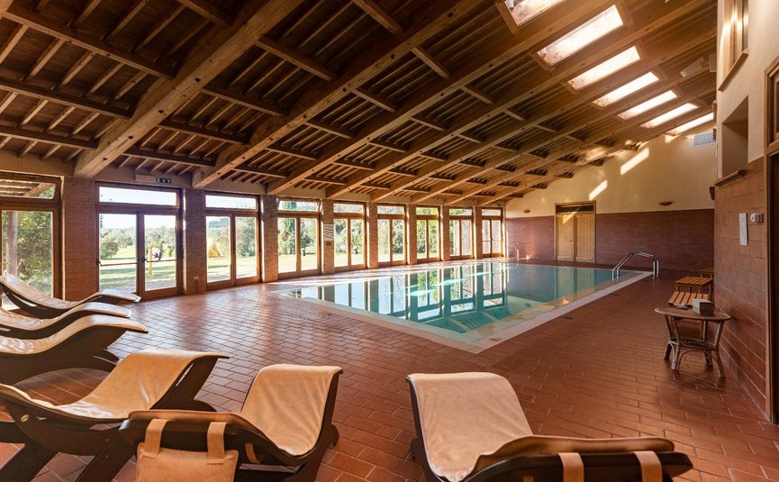 Innenansicht eines Schwimmbads mit Holzdecke und Liegestühlen