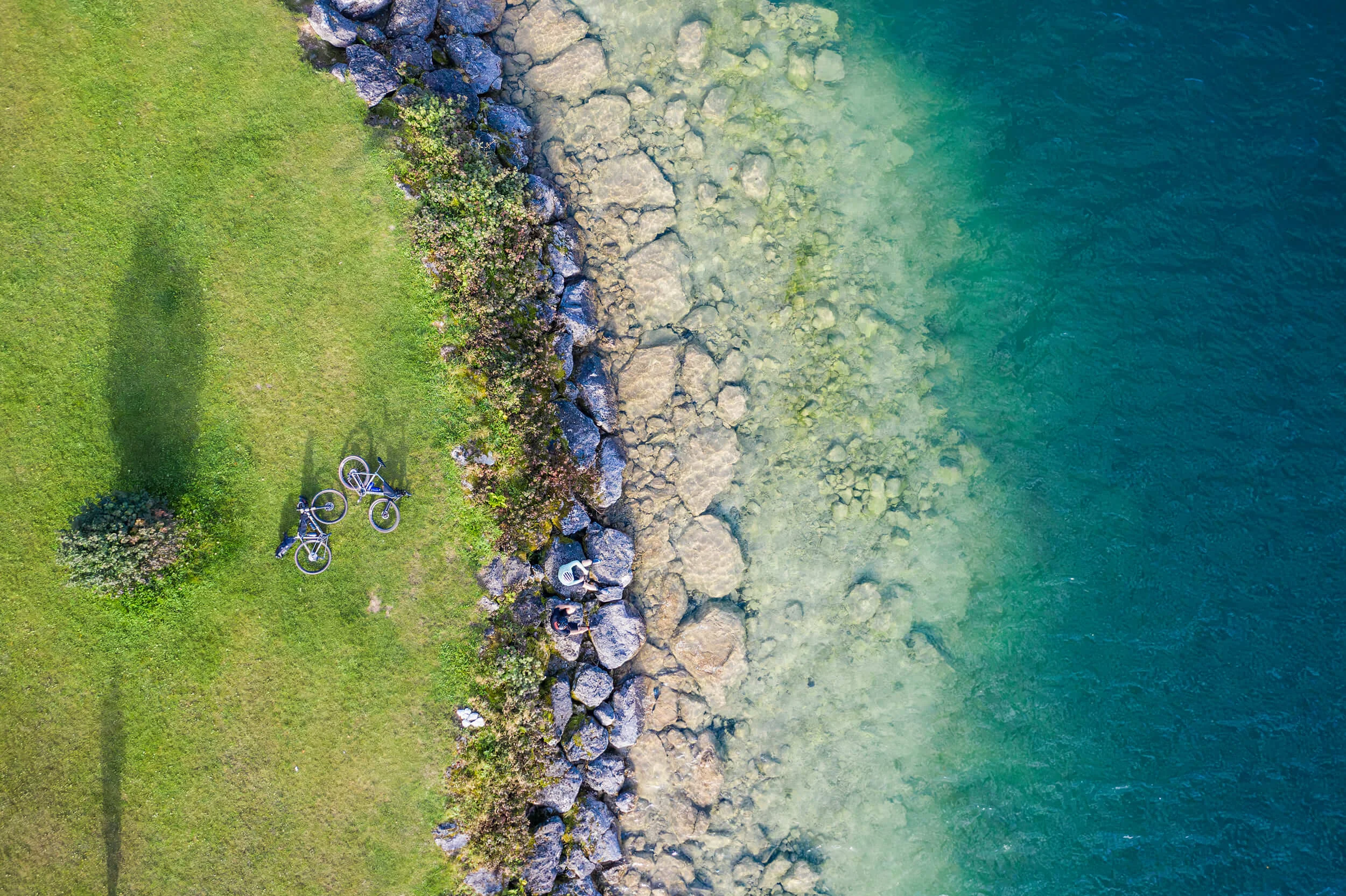 Drei Seen, eine Gravelrunde: Die 3-Seen-Tour ab Fuschl © Heiko Mandl Zwei Fahrräder und Personen auf Felsen an klarem See neben grünem Gras