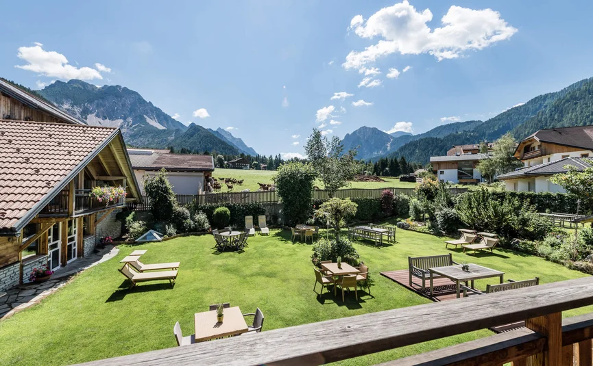 Blick auf einen Garten mit Tischen, Stühlen und Bergen im Hintergrund