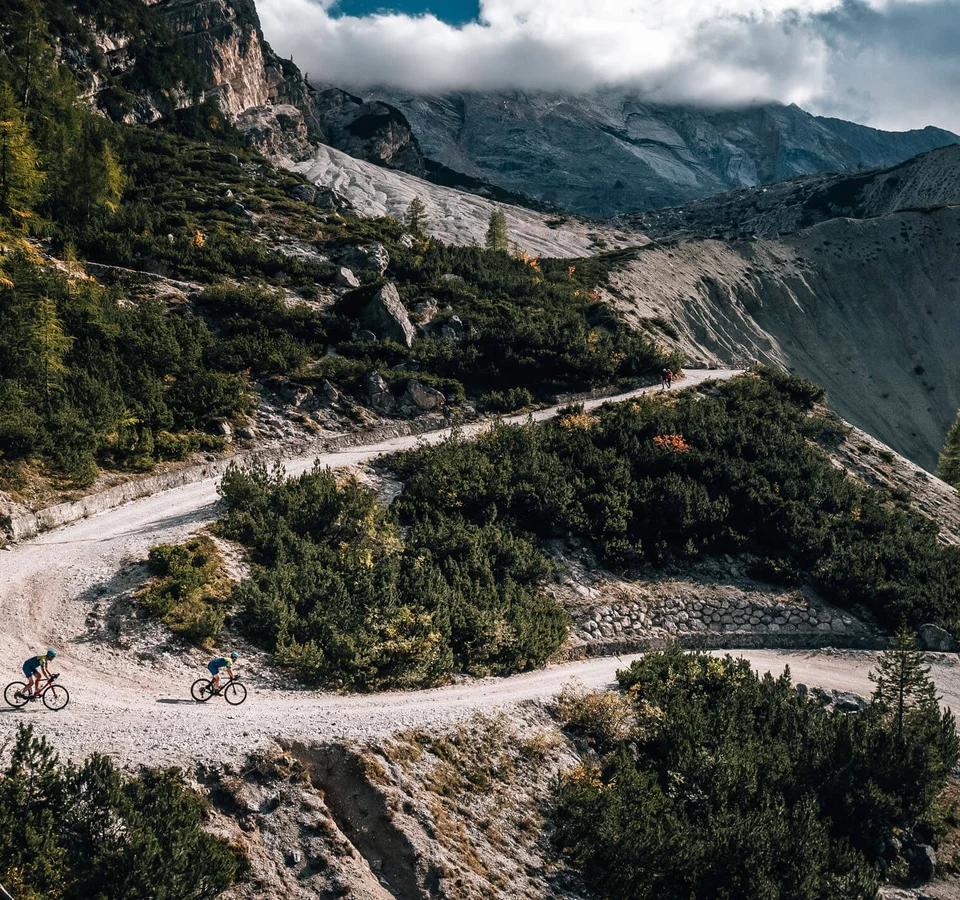 Zwei Radfahrer auf kurviger Bergstraße in bewaldeter Landschaft