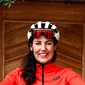 Woman in red cycling outfit thumbs up in front of wooden door with bike