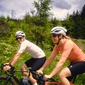 Two cyclists riding on a road with forest greenery in the background