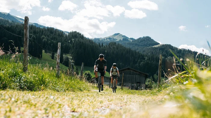 Graveln in den Kitzbüheler Alpen © Martina Wunderle / Flo Distl Zwei Radfahrer fahren auf einem Weg in den Bergen an einem sonnigen Tag