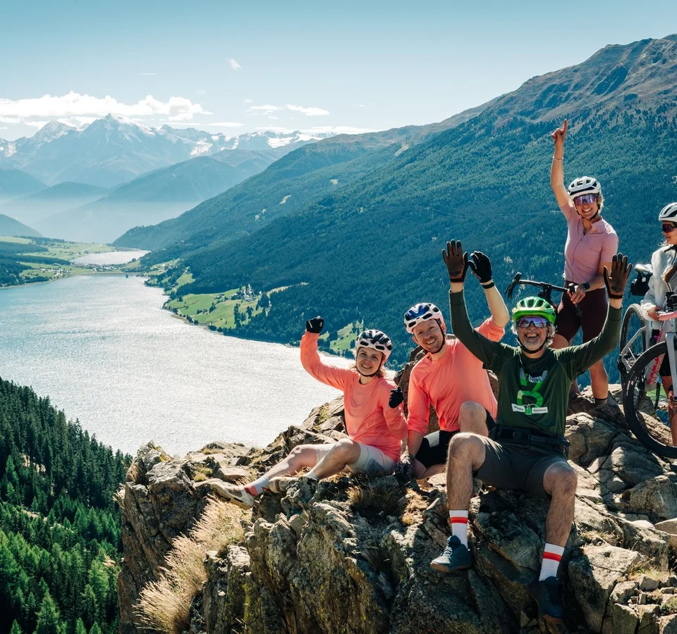 Das waren die Golden Days in Nauders © TVB-Tiroler-Oberland-Nauders-Christian-Penning Eine Gruppe Radfahrer jubelt auf einem Felsen über einem türkisfarbenen Bergsee