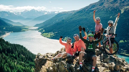 Das waren die Golden Days in Nauders © TVB-Tiroler-Oberland-Nauders-Christian-Penning Eine Gruppe Radfahrer jubelt auf einem Felsen über einem türkisfarbenen Bergsee