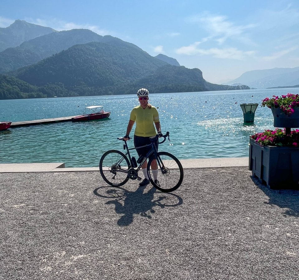 Graveln im Salzkammergut – Seen. Schotter. Sehnsucht. Fahrradfahrer am See mit Bergen im Hintergrund und klarem Himmel