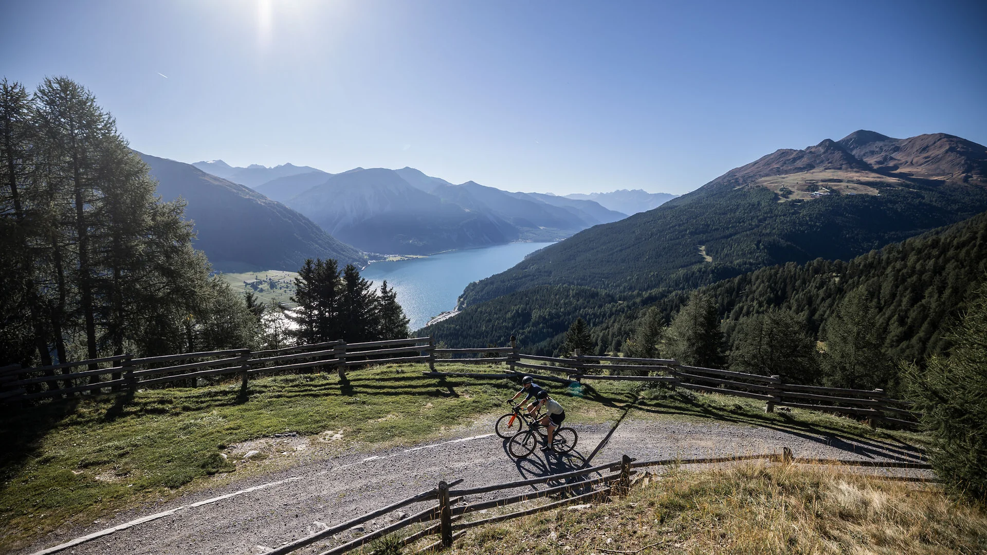 Ein Gravel-Wochenende in Nauders-Reschensee © Heiko Mandl Zwei Radfahrer auf einem Bergweg mit Blick auf See und Berge im Sonnenschein