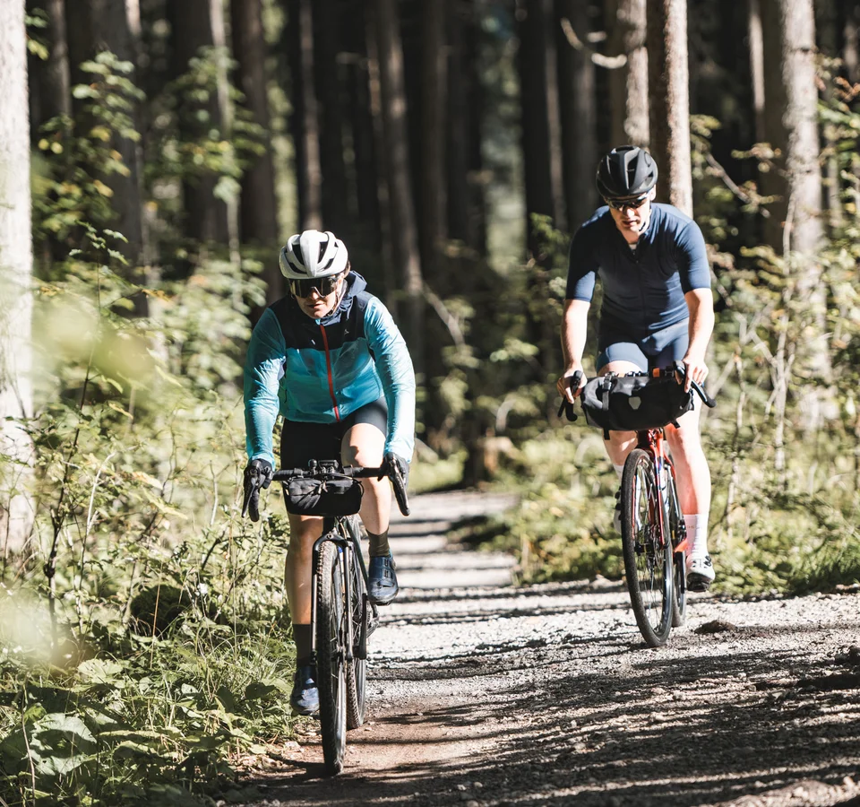Werde zum GravelKING in Gravel.Tirol © Andreas Vigl Zwei Radfahrer fahren auf einem Waldweg bei sonnigem Wetter