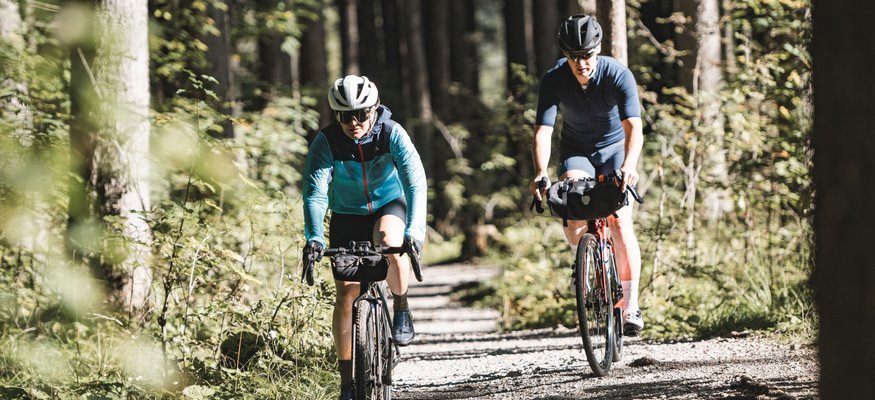 Zwei Radfahrer fahren auf einem Waldweg bei sonnigem Wetter