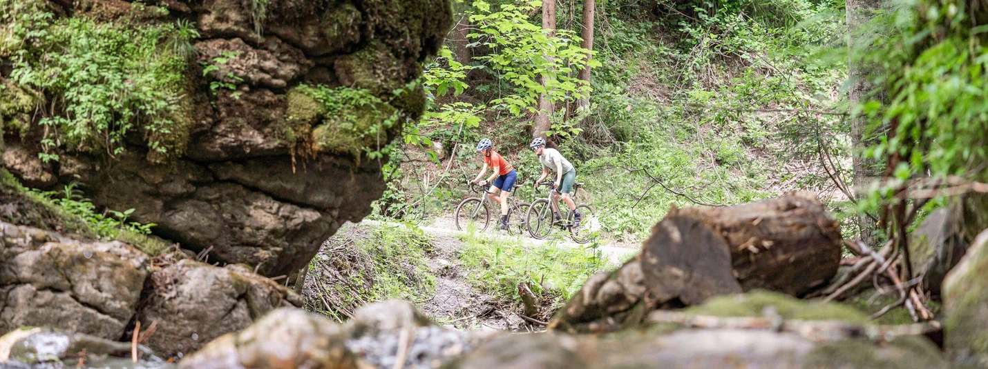 Buchensteinwand tour © Saalfelden Leogang Touristik - Yvonne Hörl Two cyclists riding on forest trail beside creek in green woodland