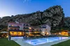Hotel with illuminated pool near rocky cliff at dusk