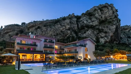 Hotel with illuminated pool near rocky cliff at dusk