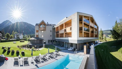 Basecamp mit Seele: Graveln im Hotel Laurin’s © Harald Wisthaler Modernes Hotel mit Pool und Sonnenliegen vor Bergkulisse bei sonnigem Himmel