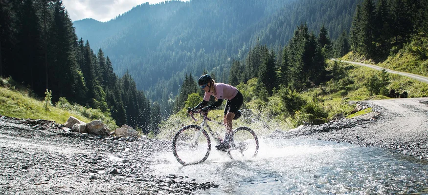 Checklist für das Bikepacking-Abenteuer © Maria Wilke Radfahrer fährt mit Mountainbike durch Wasser im Gebirge bei Sonnenschein