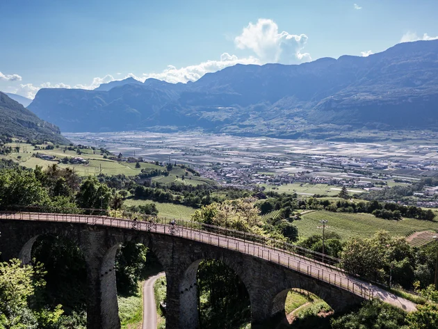 Gravel & Törggelen: Warum Tramin im Herbst perfekt für Gravelbiker ist © Heiko Mandl Fahrradfahrer auf einer Brücke mit Blick auf Tal und Berge bei klarem Himmel