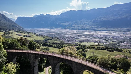 Gravel & Törggelen: Warum Tramin im Herbst perfekt für Gravelbiker ist © Heiko Mandl Fahrradfahrer auf einer Brücke mit Blick auf Tal und Berge bei klarem Himmel
