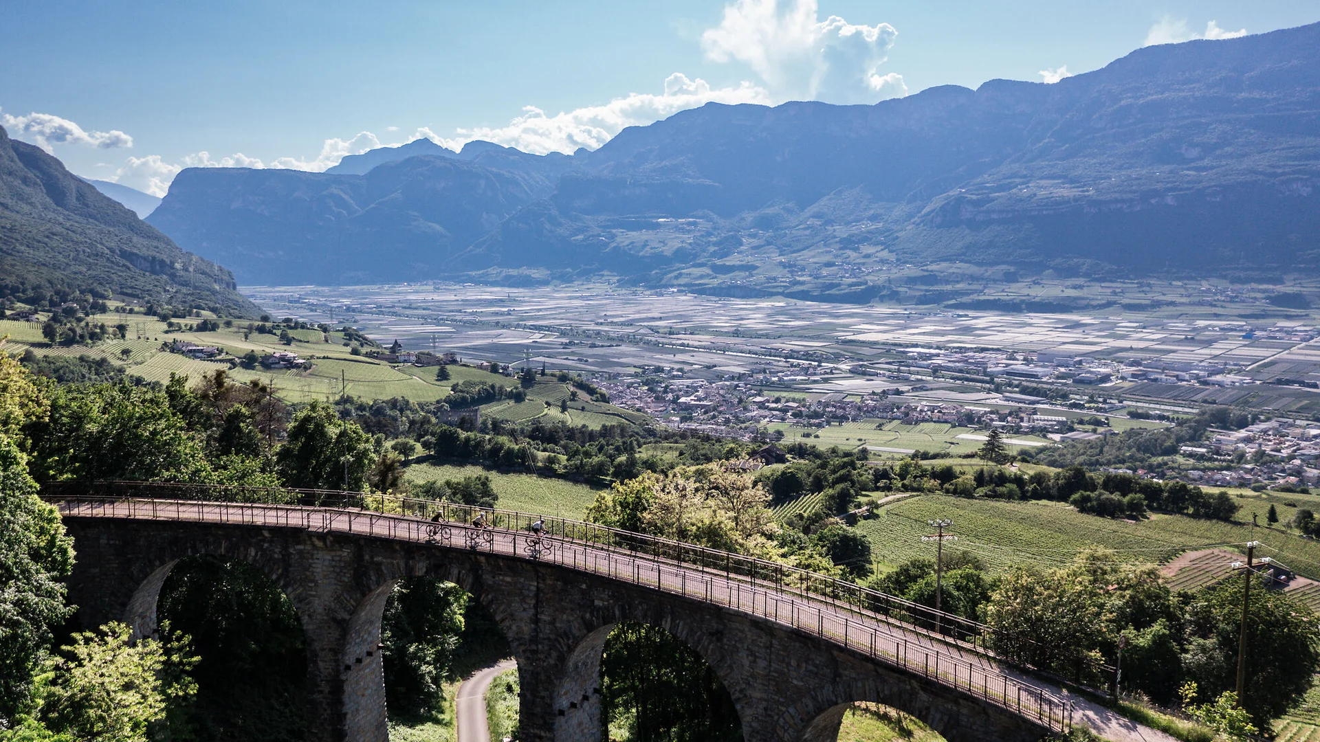 Fahrradfahrer auf einer Brücke mit Blick auf Tal und Berge bei klarem Himmel