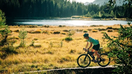Das waren die Golden Days in Nauders © TVB-Tiroler-Oberland-Nauders-Christian-Penning - Gravelbiken in Nauders im Herbst Mountainbiker auf einem Holzsteg am See, umgeben von Wiesen, Wald und Bergen