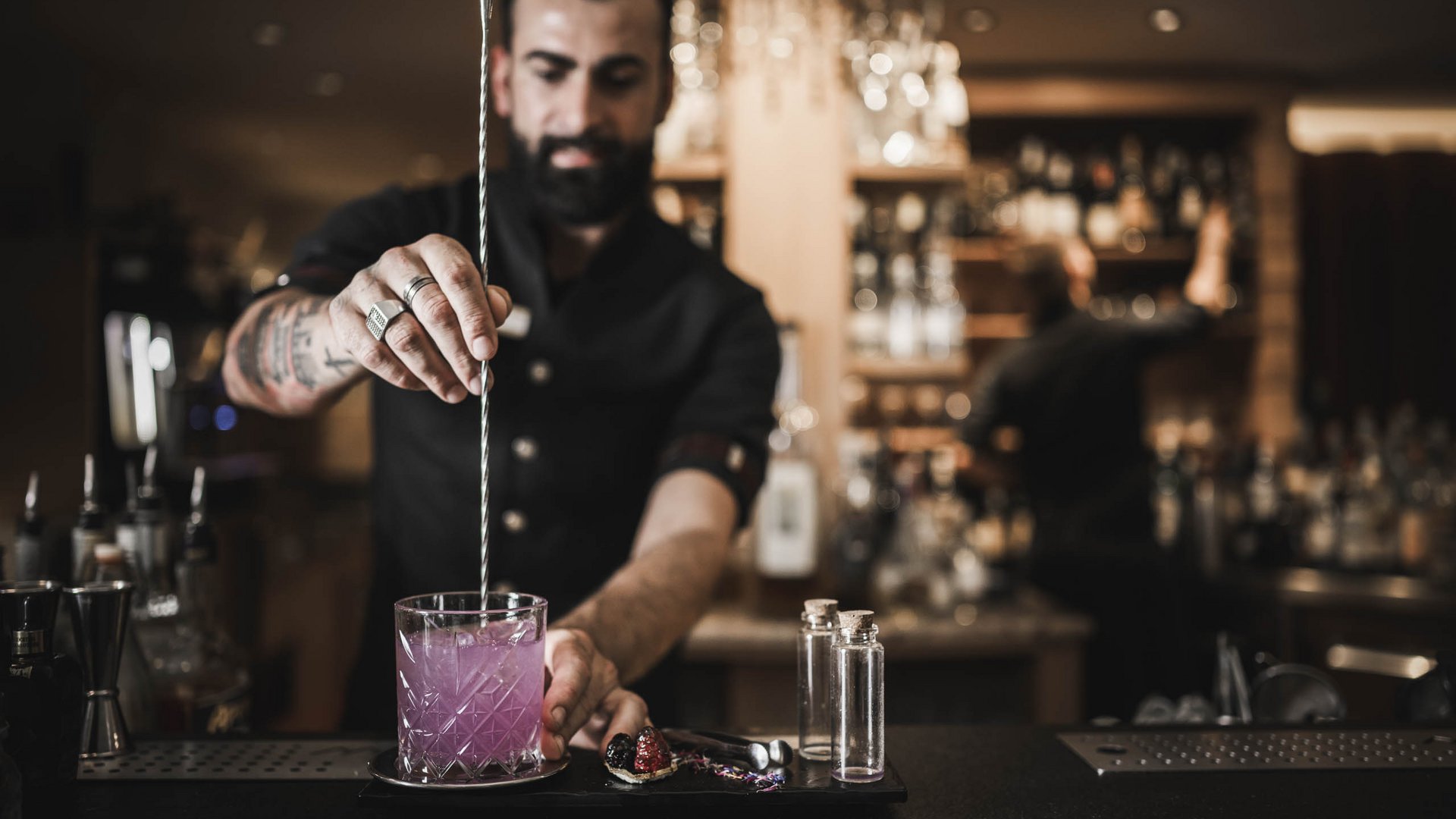 Barkeeper rührt pinkfarbigen Cocktail in Bar mit langem Löffel