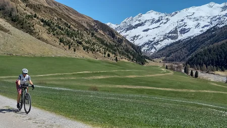 Radfahrer auf Bergweg mit grüner Wiese und schneebedeckten Gipfeln