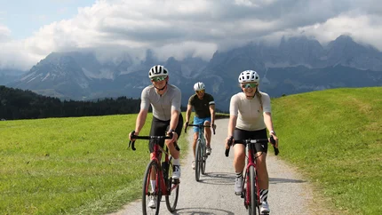 Drei Radfahrer auf einem Weg mit Bergen und Wolken im Hintergrund