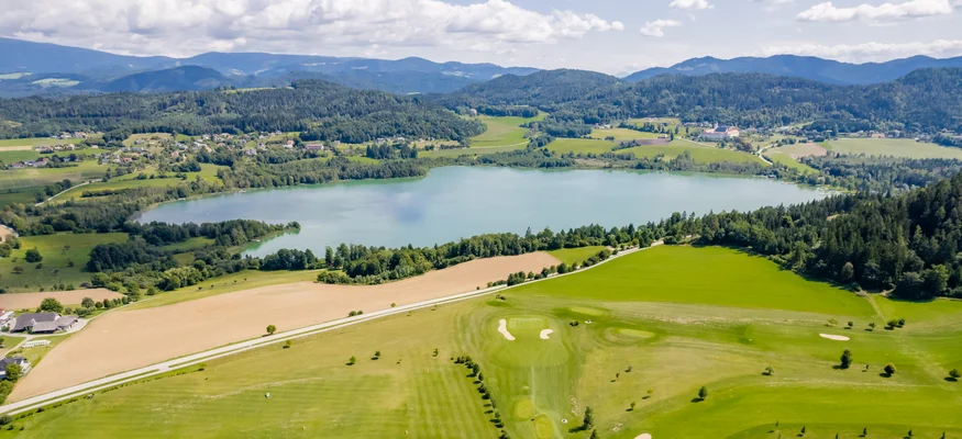 Luftaufnahme eines Golfplatzes mit See und bewaldeten Hügeln im Hintergrund