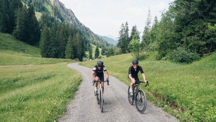 Zwei Radfahrer fahren auf einem Schotterweg durch eine grüne Berglandschaft