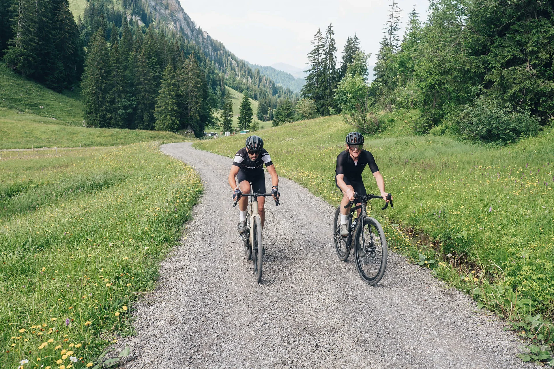 Gravelbike Holidays © Ian Ehm - Vorarlberg Tourismus Zwei Radfahrer fahren auf einem Schotterweg durch eine grüne Berglandschaft