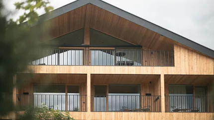 Modern wooden house facade with balconies and glass windows under cloudy sky