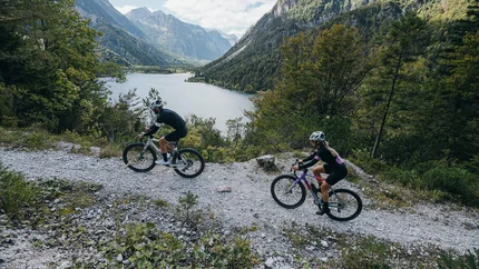Two cyclists on mountain trail with lake and mountains in background