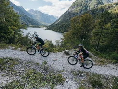 Two cyclists on mountain trail with lake and mountains in background