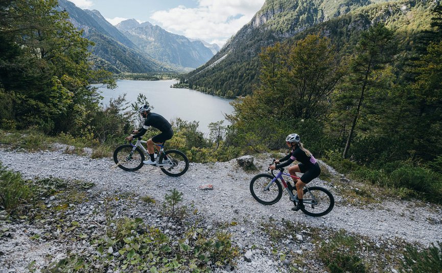 Gravel bike holiday on Lake Wörthersee © WRTG Fotograf Sam Strauss Two cyclists on mountain trail with lake and mountains in background