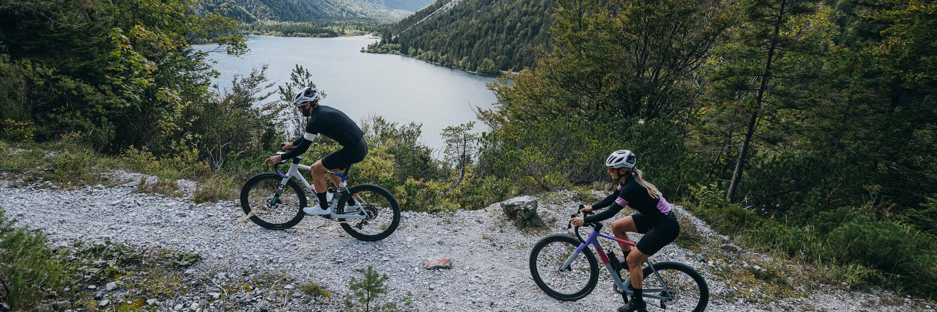 Two cyclists on mountain trail with lake and mountains in background