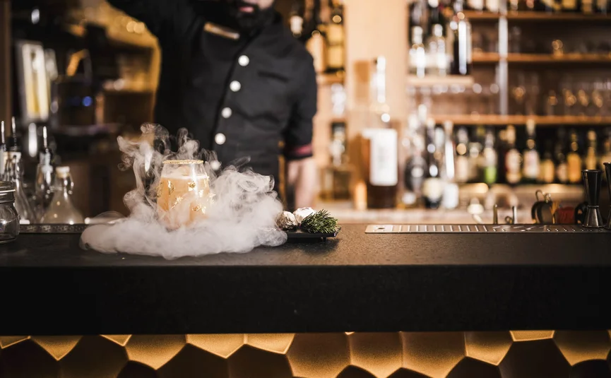 Excelsior Dolomites Life Resort ****S © Hannes Niederkofler Barkeeper bereitet rauchigen Cocktail in stilvoller Bar zu