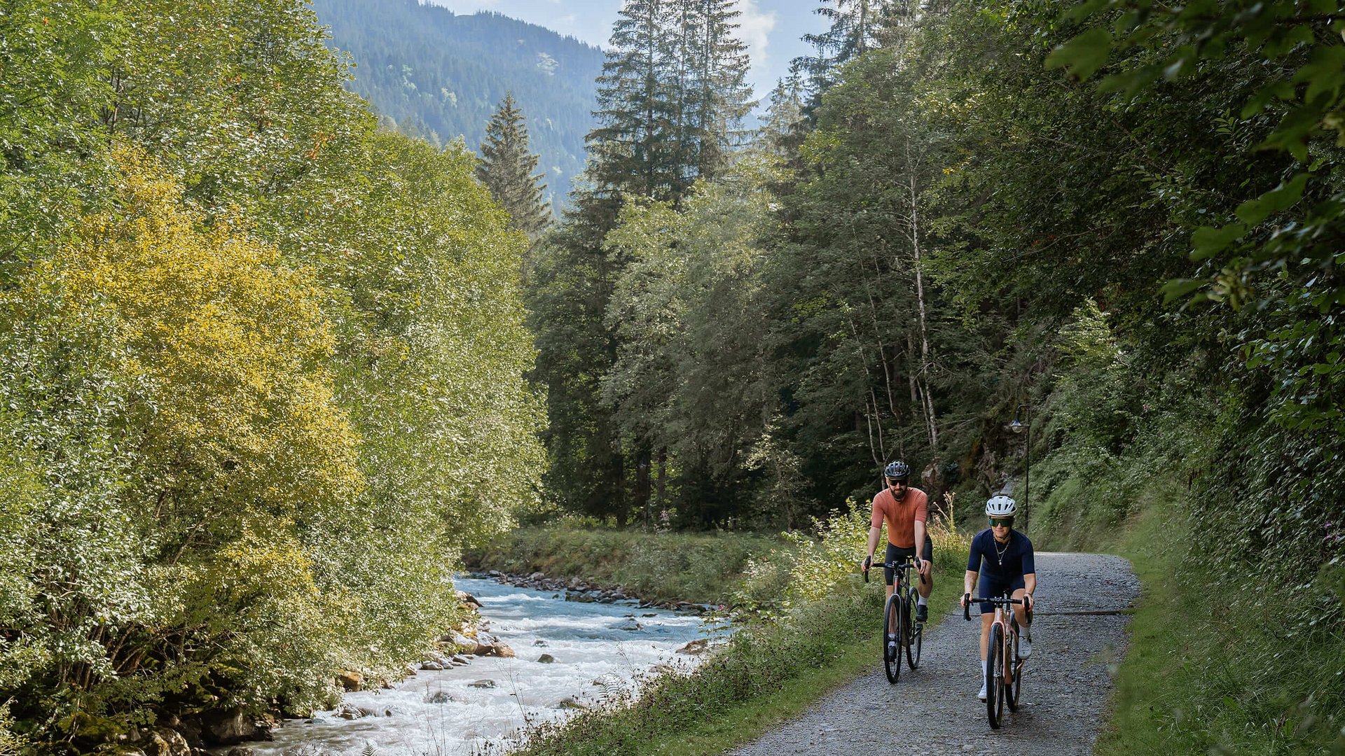 Zwei Radfahrer auf einem Waldweg neben einem Fluss in den Bergen