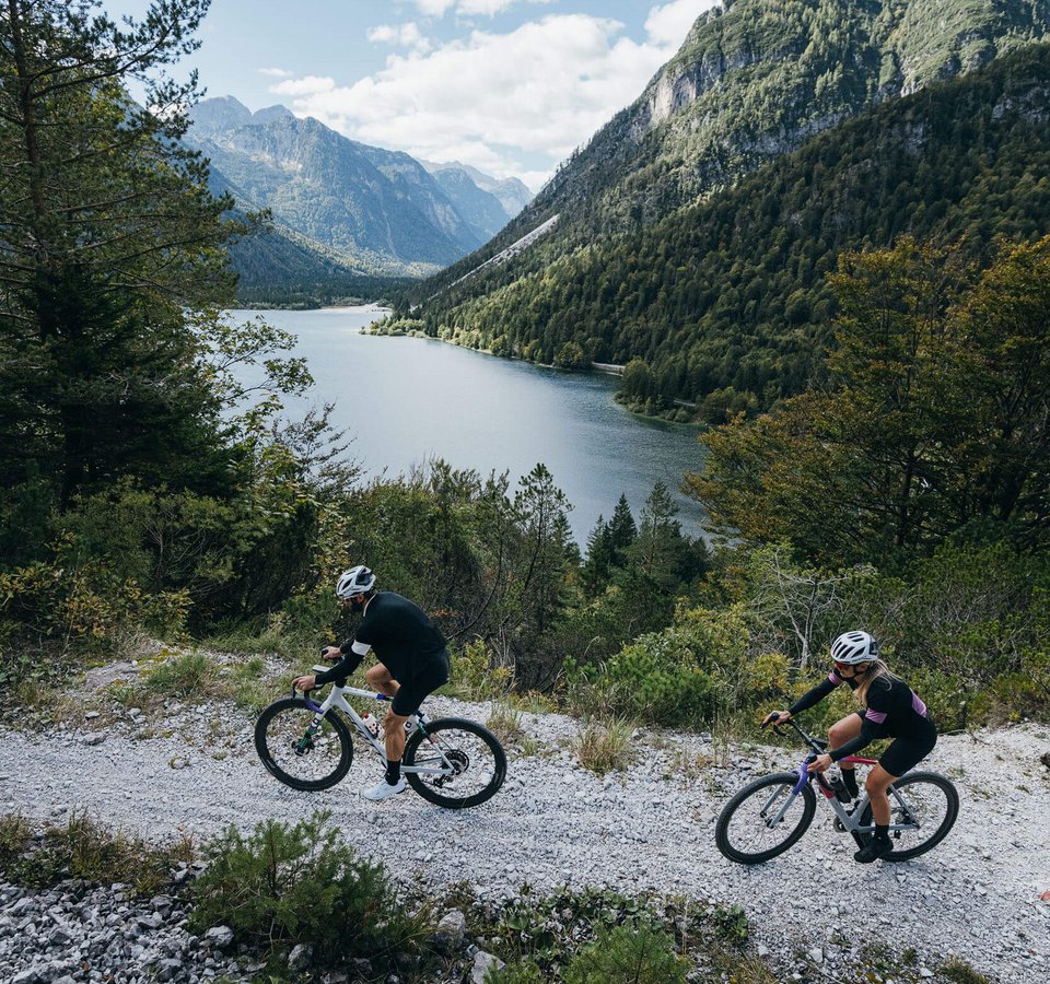 Zwei Radfahrer fahren auf einem Bergweg neben einem See