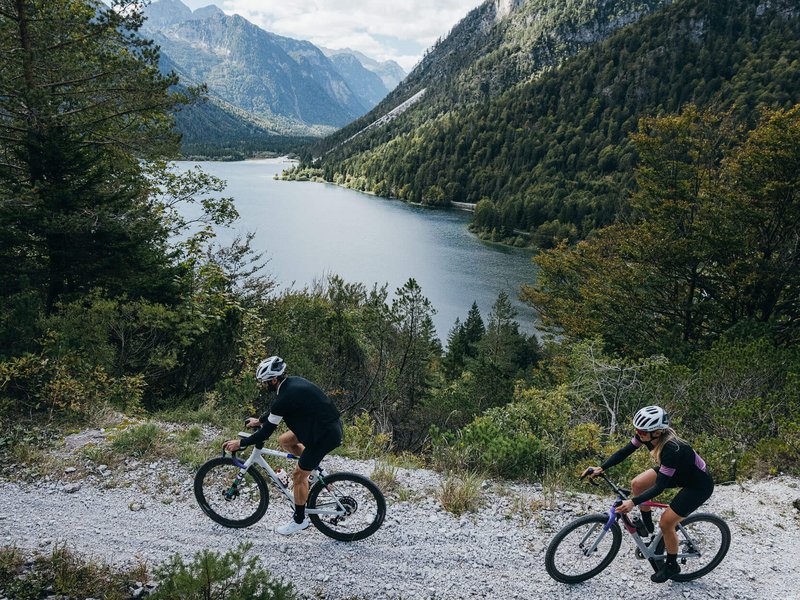 Zwei Radfahrer fahren auf einem Bergweg neben einem See