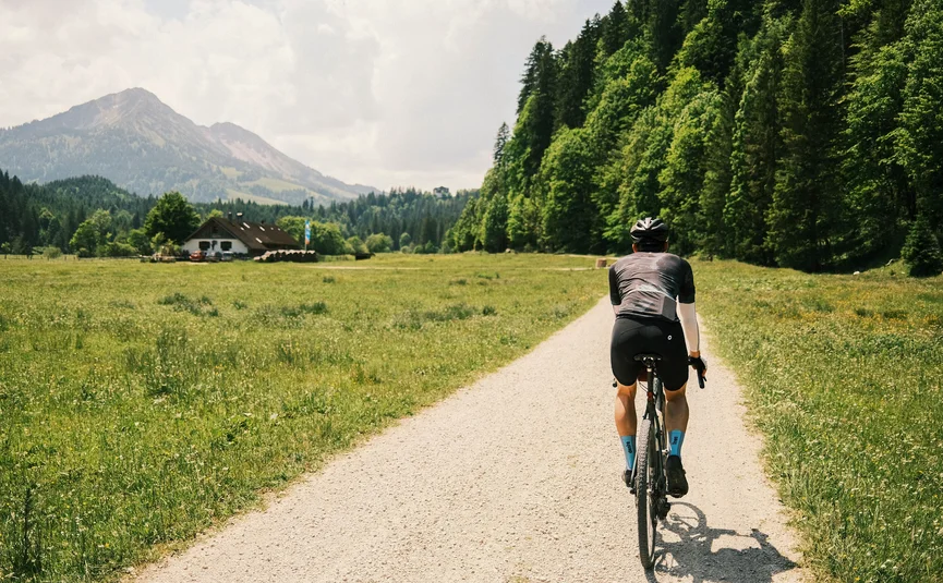 Fahrradfahrer auf einem Weg durch eine grüne Wiese mit Bergen im Hintergrund